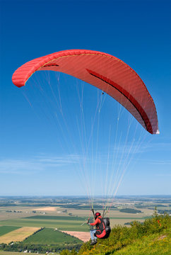 Paraglider with red parachute taking off from the hill