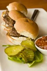 Three small burgers with condiments on a platter