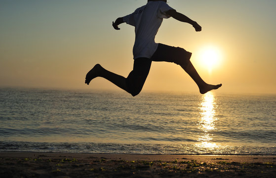 Young Boy Jumping On Beach At Sunrise