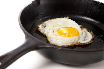 A fried egg in a black iron skillet on a white background,