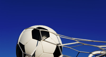 A soccer ball or football in a goal net in front of a blue sky