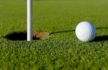 A white golf ball near the hole of a golfing green or course