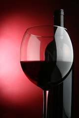 Glass and bottle of wine over red background
