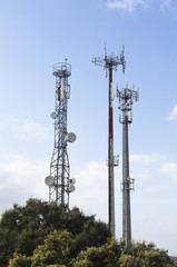 Three telecommunication antennas against a clear blue sky.