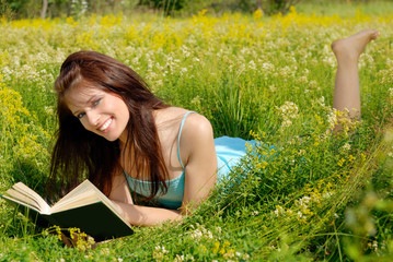 A smiling girl lying in a meadow with a book.