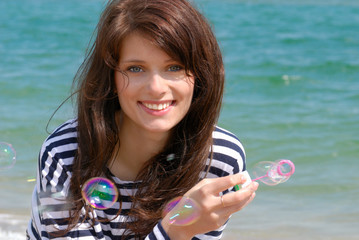 Young woman portrait making soap bubbles on the sea background