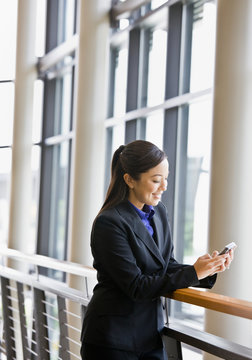Businesswoman leaning on railing in office and text messaging