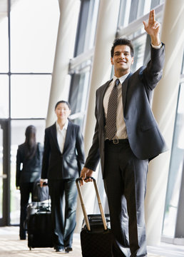 Business traveler pulling suitcase and gesturing to co-worker