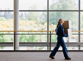 Side view of delivery woman in uniform carrying stack of boxes