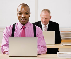 Businessman typing on laptop with co-worker in background