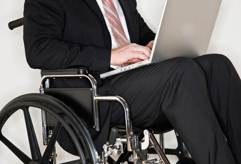 Disabled businessman sitting in wheel chair typing on laptop - Powered by Adobe