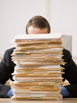 Frustrated Businessman Looking At Pile Of File Folders