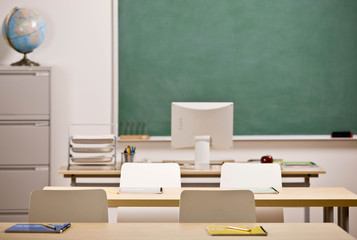 Desks, chairs, blackboard and computer in empty school classroom
