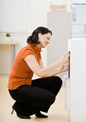 Fototapeta na wymiar Businesswoman kneeling and filling glass at water cooler