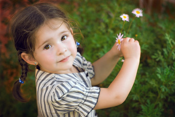Beautiful little girl picking a daisy in the yard