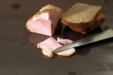 Slit ham and rye bread with kitchen knife on glassy table