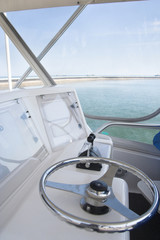 A close-up view of the cockpit of a modern yacht, featuring a polished chrome steering wheel,...