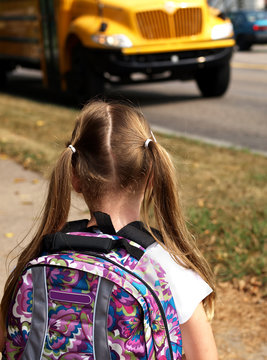 young girl wearing a backpack and waiting for school bus