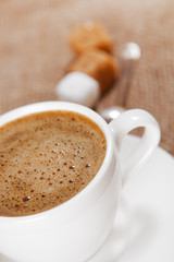 Cup of black coffee with froth on brown background, shallow DOF