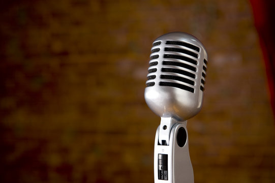A silver vintage microphone in front of a blurred red brick wall
