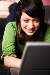 A beautiful asian girl relaxing on the sofa working on laptop