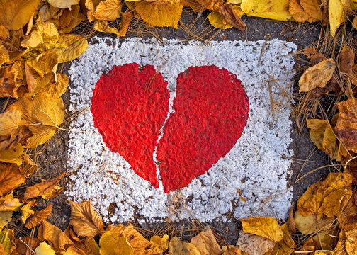 Broken red heart painted on the road in a dry leaves frame