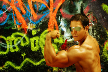 Bodybuilder flexing bicep against graffiti