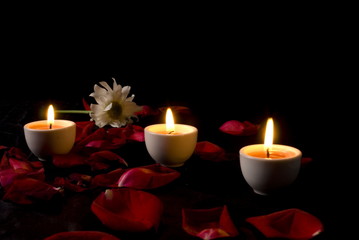 Three Candles burning and red rose petals .
