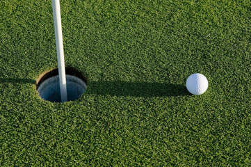A white golf ball near the hole of a golfing green or course