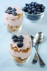 Glasses of muesli with fruit yoghurt, topped with blueberries.