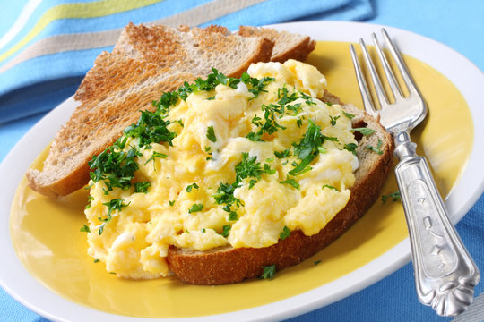 Scrambled eggs garnished with parsley, with sourdough toast.