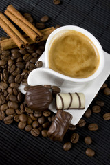 Cup of coffee with chocolate candies and cinnamon sticks