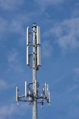 Gray cell tower over whispy clouds and blue sky