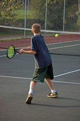 A teenage boy prepares to backhand the tennis ball
