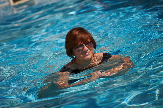 Happy active senior woman ( 60s ) swimming in pool