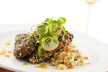 Gourmet salmon dish garnished with vegetables, white background.