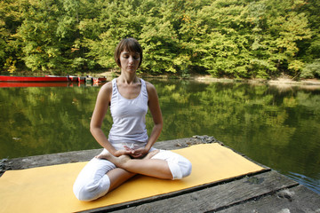 Naklejka na ściany i meble Woman doing yoga on lake in park in autumn