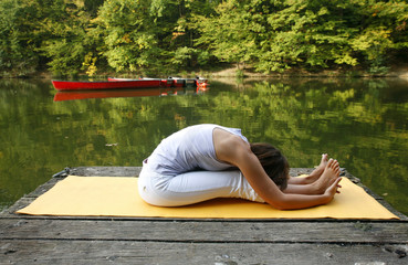 Woman doing yoga on lake in park in autumn