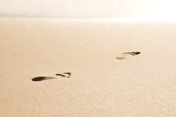 Fototapeta na wymiar footprints on sand surface heading towards bright sunlight