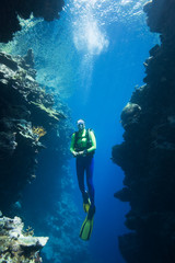 scuba diver swimming between two coral cliffs, underwater