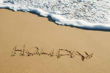 'holiday' written onto sand surface about to be washed away