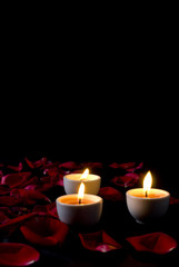 Three Candles burning and red rose petals .