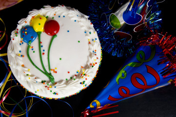 A white birthday cake surrounded by colorful party hats