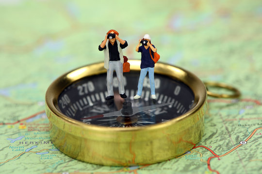 Miniature tourists taking pictures while standing on a compass
