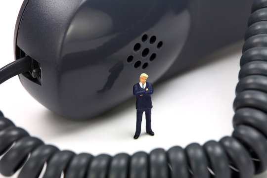 Miniature Businessman Stands In Front Of A Phone Receiver.