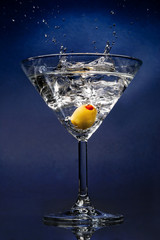 Cocktail with an olive splash on blue background