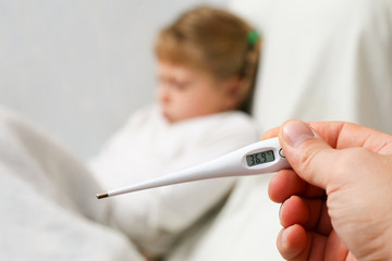 Young girl in bed. Thermometer in hand close up