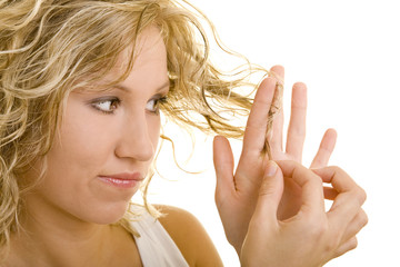 Blonde Frau schaut sich kritisch ihre Haarspitzen an