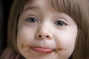 Little girl with face covered in chocolate looking at the camera