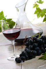 Glass of red wine, decanter and fresh cut black wine grape